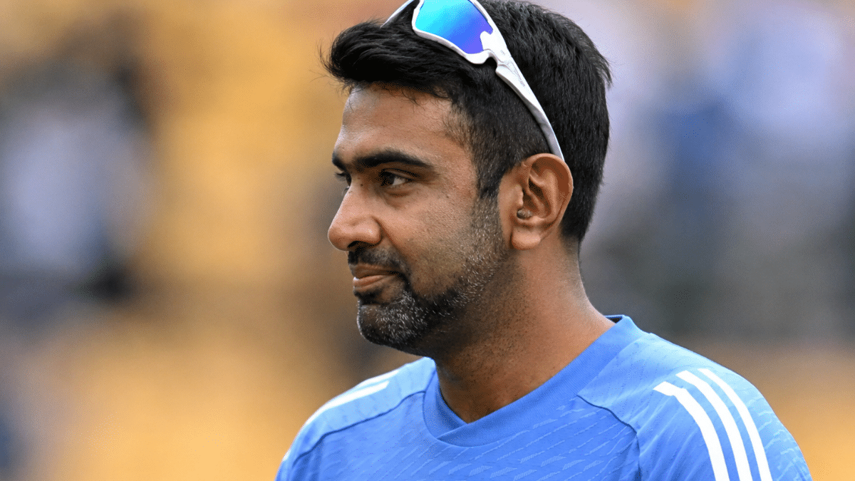 Close-up portrait of R Ashwin in blue training jersey with sunglasses on head, looking to the side against a blurred background.