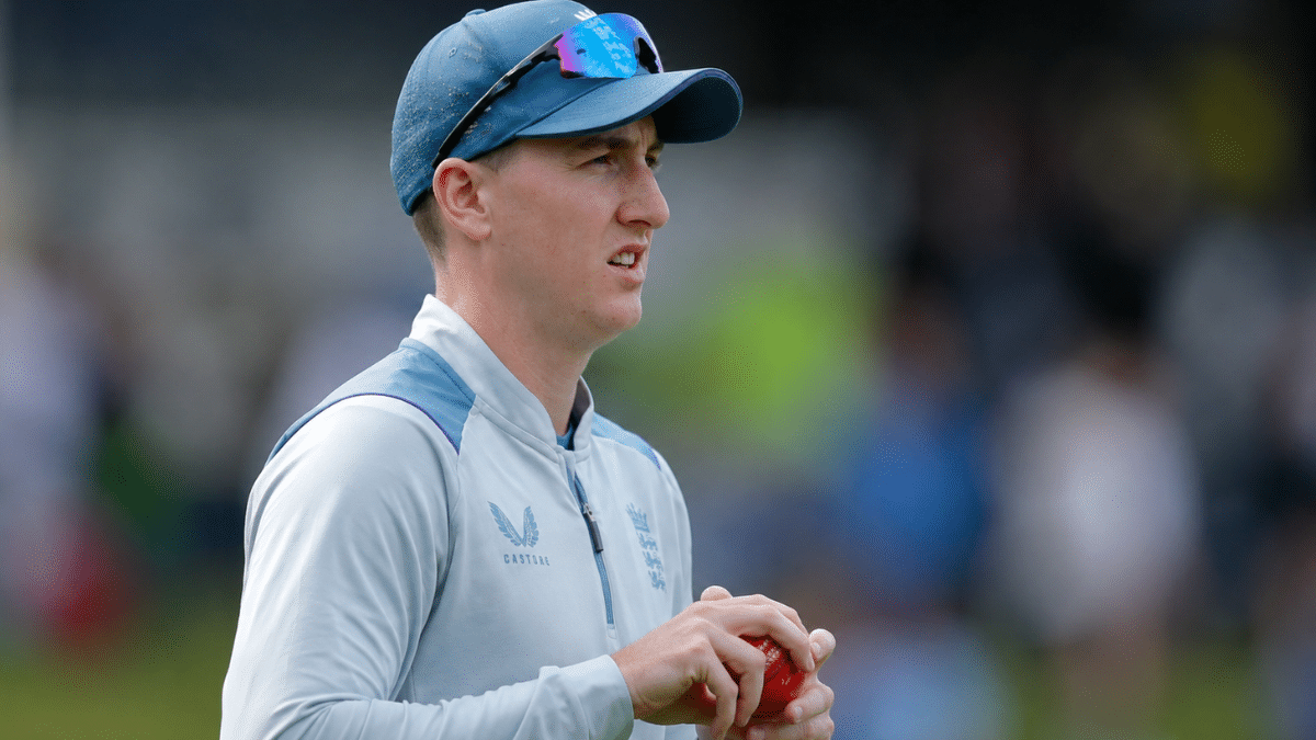 Harry Brook holding a red cricket ball during training session, captured in side-profile view on a cricket ground with a blurred stadium background.