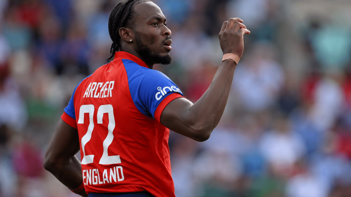 Ultra-realistic rear side-angle photograph of Jofra Archer celebrating during an England cricket match, captured with a shallow depth of field and blurred crowd.
