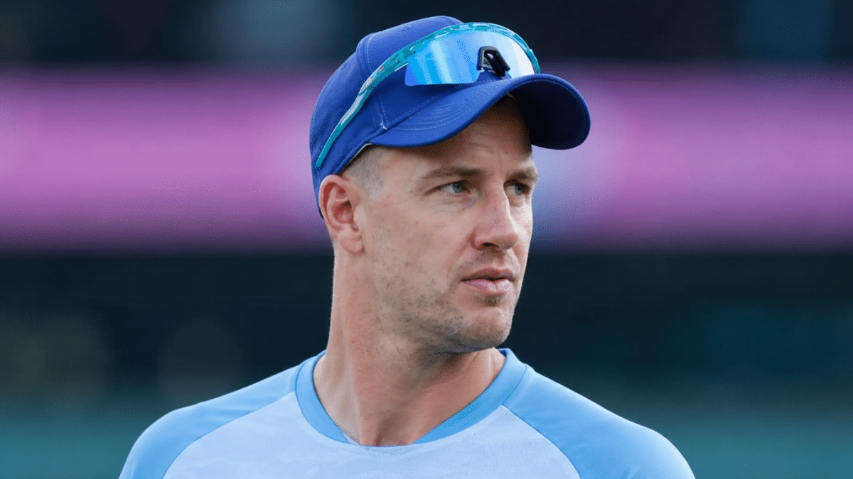 Morne Morkel in blue training jersey and cap during a stadium practice session, side-angle portrait with blurred cricket ground background.