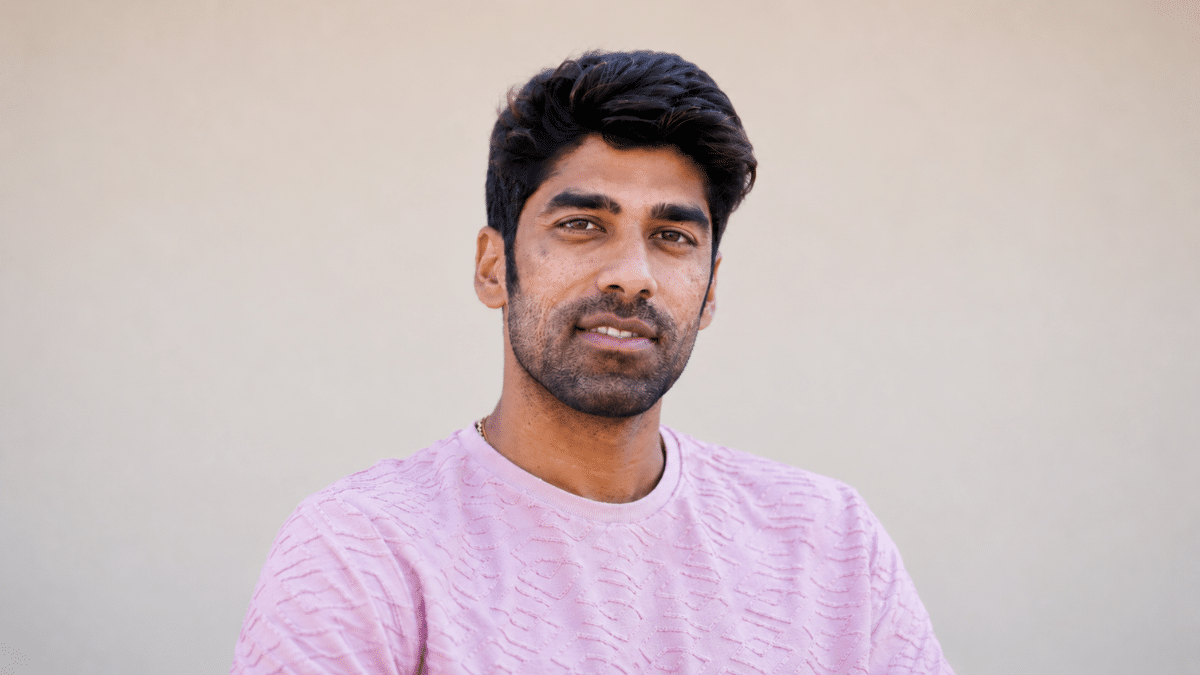 Shashank Singh poses for a portrait wearing a light pink textured T-shirt against a blurred neutral background, looking directly at the camera with a slight smile.