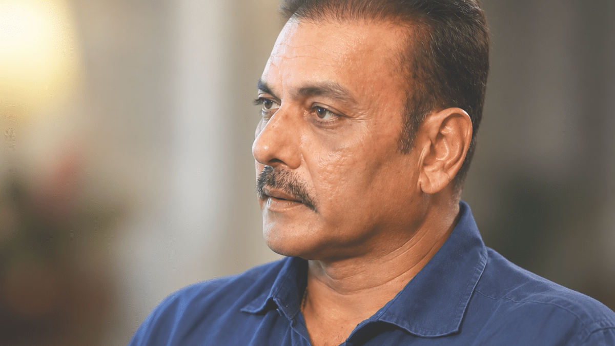 Ultra-realistic side-profile portrait of Ravi Shastri in a navy blue shirt, captured in an editorial interview setting with a shallow depth of field.