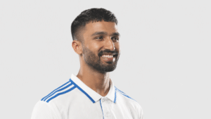 Devdutt Padikkal smiling in a three-quarter angle while wearing a white cricket jersey with blue stripes