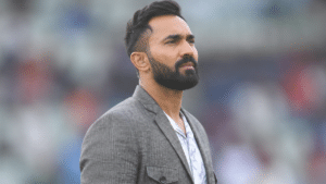 Indian cricketer wearing a gray blazer and floral shirt, standing in a stadium and looking to the side.