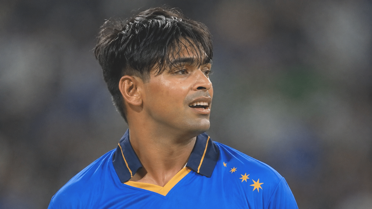 Kartik Tyagi in a blue cricket jersey, shown in side profile while looking toward the right during a cricket match.