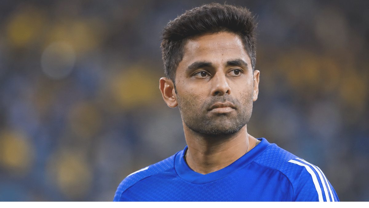 Suryakumar Yadav wearing a blue cricket jersey, looking toward the right in a three-quarter angle, with a softly blurred stadium background.
