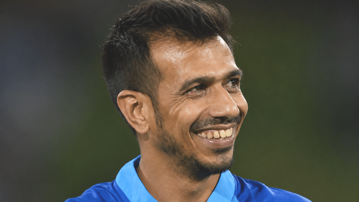 Yuzvendra Chahal smiling in a blue cricket jersey and looking to the side during a match.
