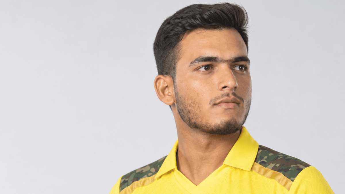 Prashant Veer in a yellow cricket jersey, shown in a right-facing three-quarter profile against a clean light gray studio background.