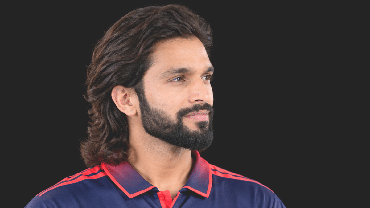 Rajat Patidar looking to the right in a three-quarter profile, wearing a navy blue and red cricket jersey against a black background.