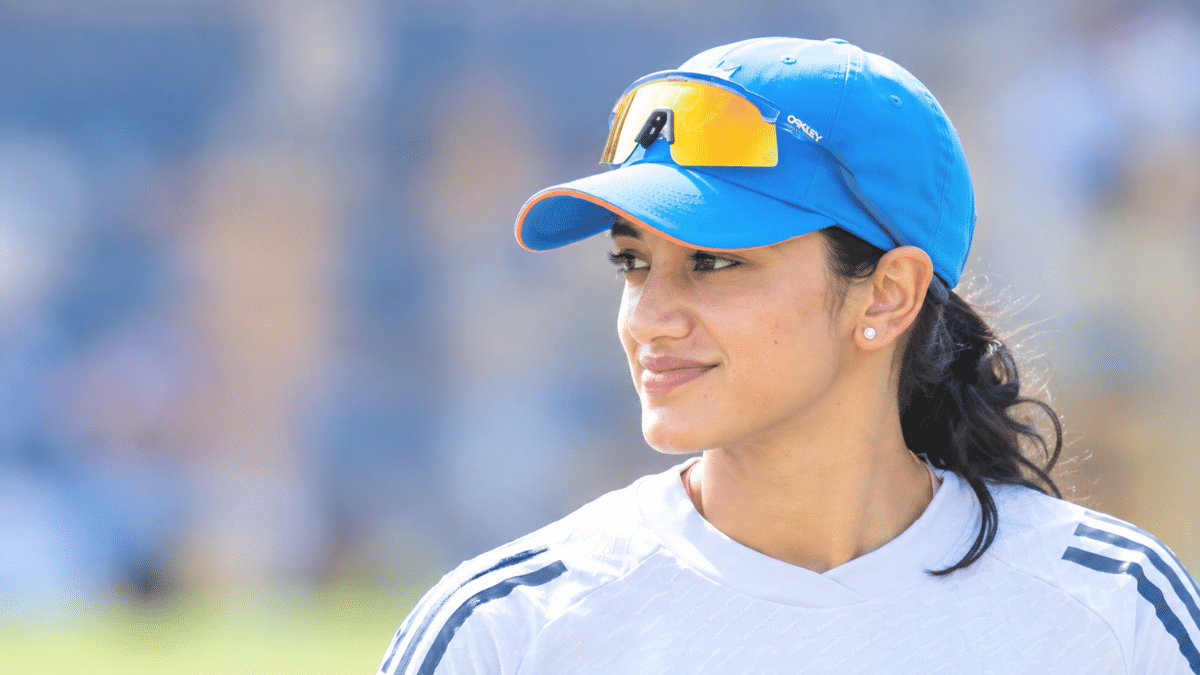 Smriti Mandhana wearing a blue cricket cap and white jersey during a cricket match.