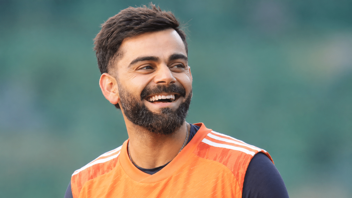Virat Kohli, Indian cricketer, smiling in an orange training jersey and looking to the side.