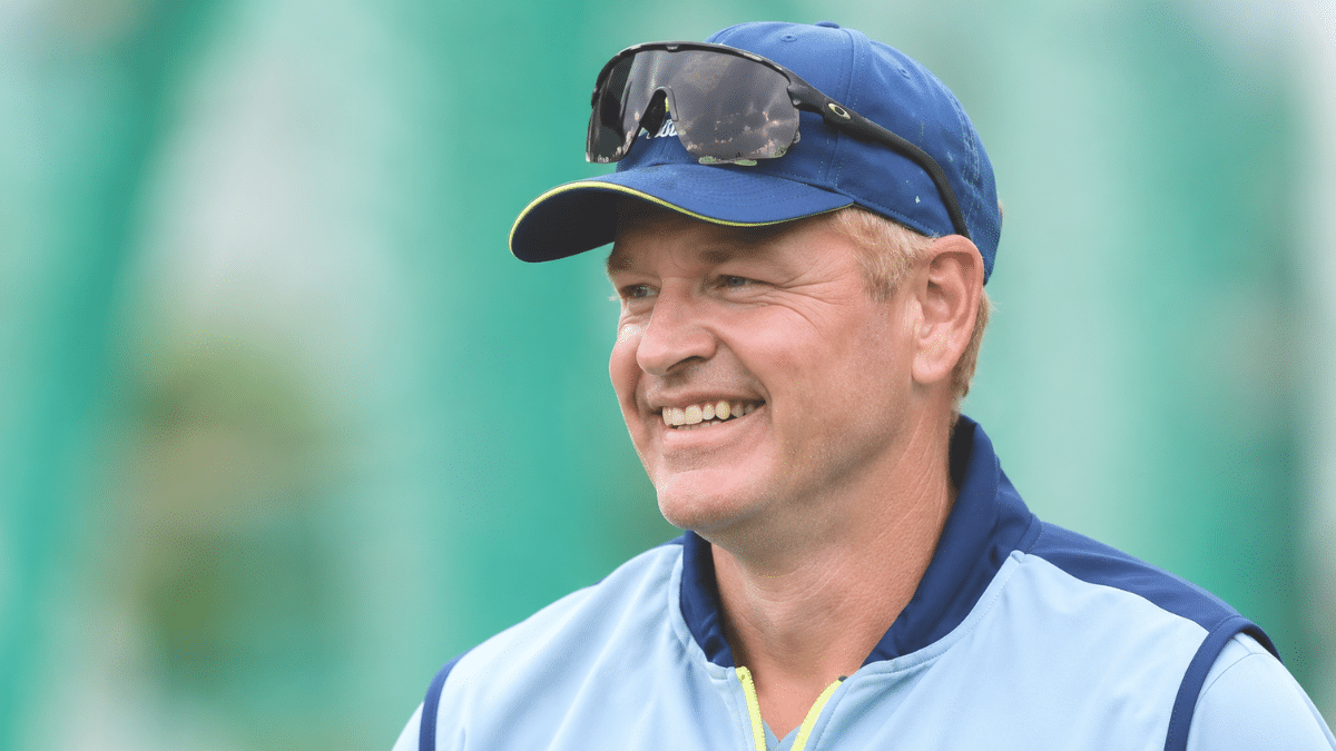 Andrew McDonald, Australian cricket coach, smiling in a light blue training jacket and navy cap.