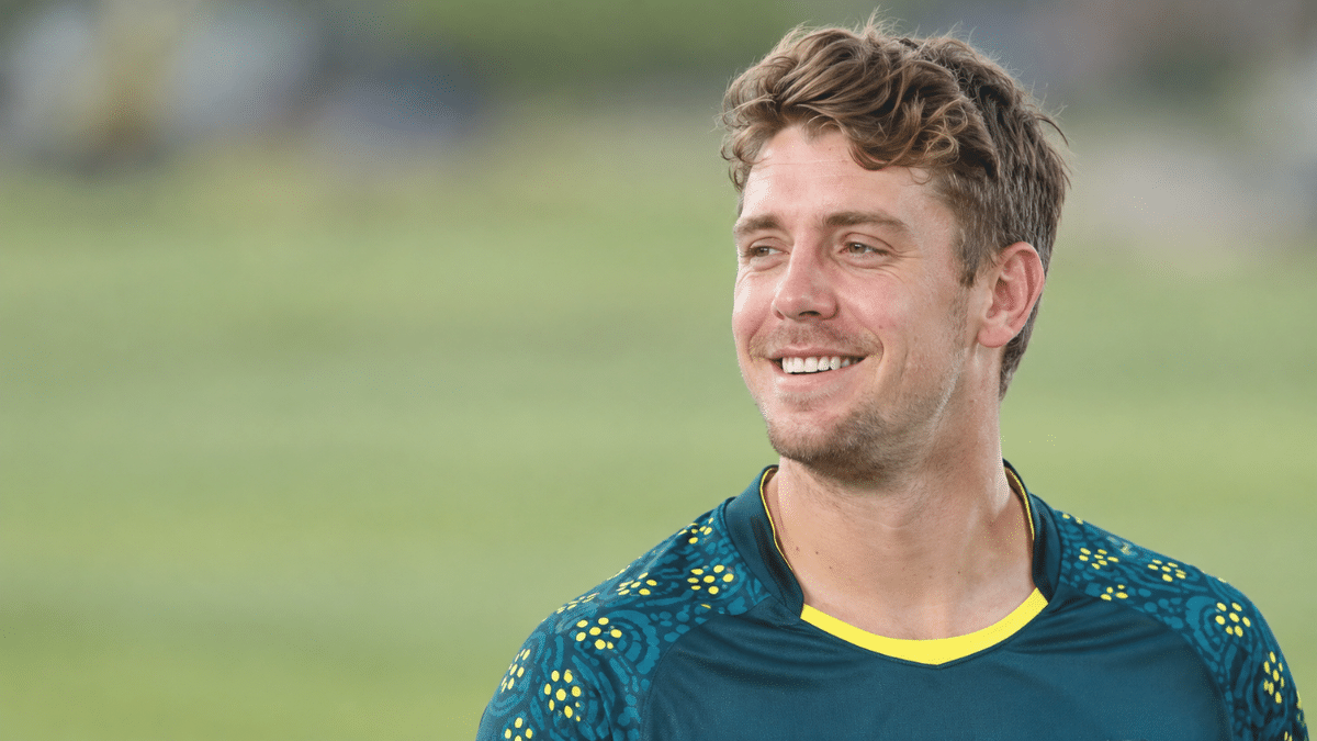 Cameron Green, Australian cricket all-rounder, smiling in a dark teal cricket jersey and looking to the left.