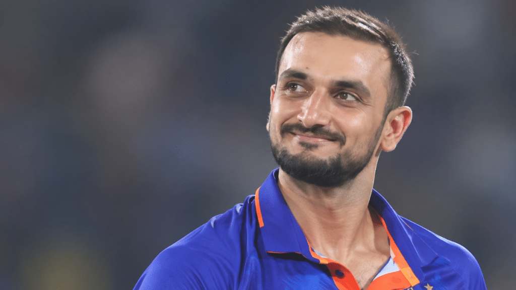 Harshal Patel, Indian right-arm medium-pacer, wearing a blue cricket jersey with orange trim and looking to the right against a blurred stadium background.