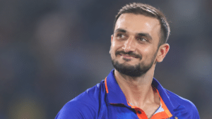 Harshal Patel, Indian right-arm medium-pacer, wearing a blue cricket jersey with orange trim and looking to the right against a blurred stadium background.