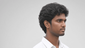 Hasan Mahmud looking slightly to the right, with curly dark hair and light facial hair, wearing a white collared shirt against a plain light gray background.