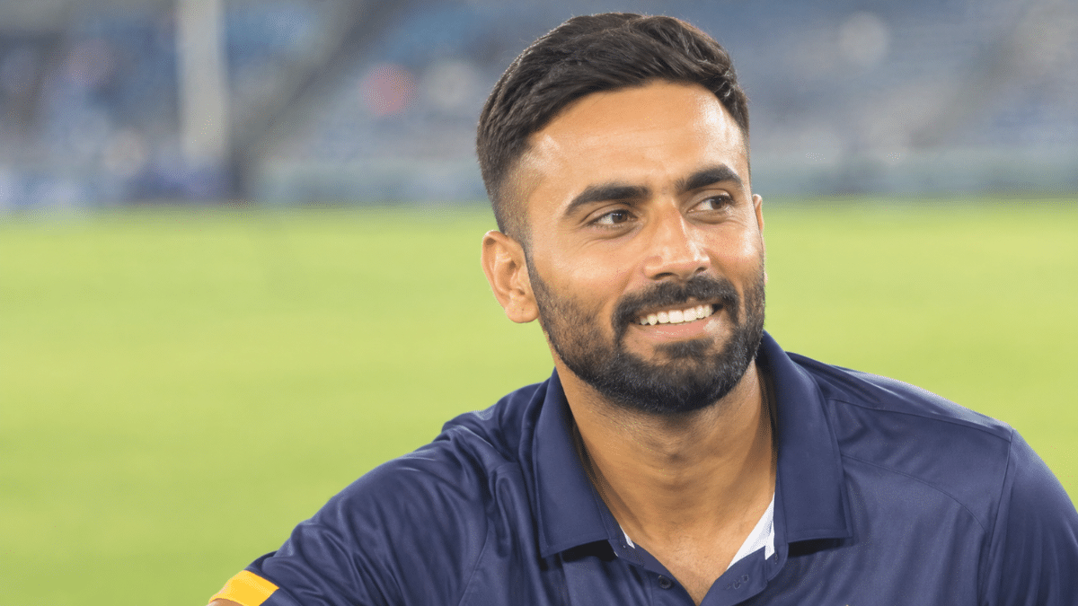 Naman Dhir, Indian right-handed batting all-rounder, smiling in a dark navy cricket jersey.
