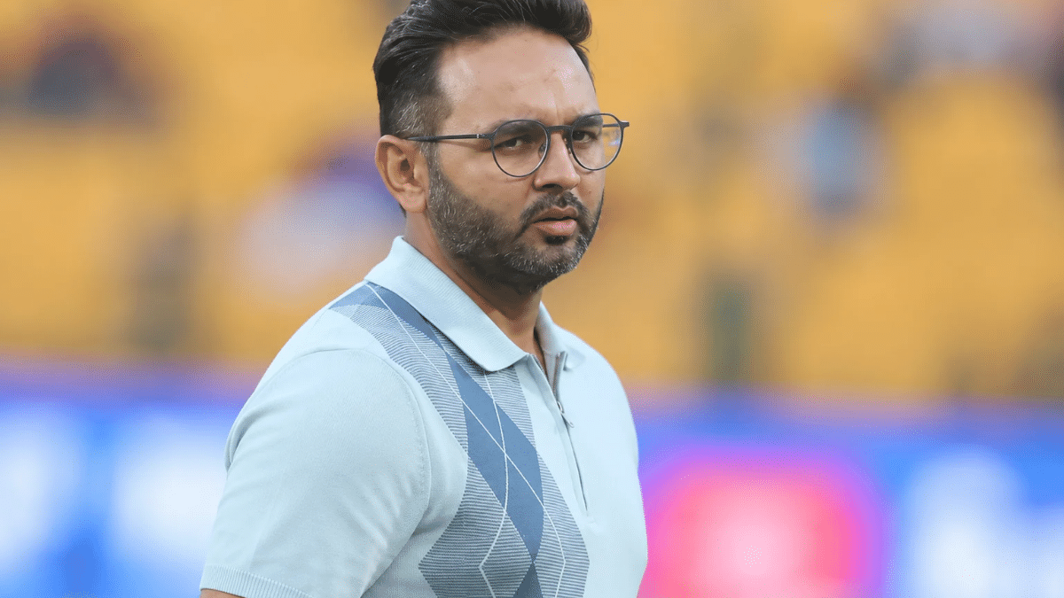 Parthiv Patel wearing glasses and a light blue polo shirt, standing at a cricket stadium