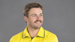 Josh Inglis, Australian wicketkeeper-batter, wearing a bright yellow cricket jersey with green trim and looking to the right against a clean gray background.