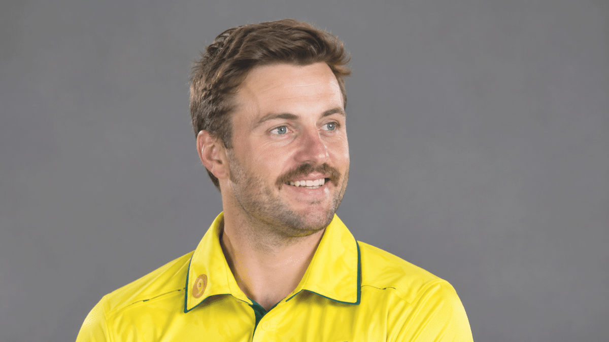 Josh Inglis, Australian wicketkeeper-batter, wearing a bright yellow cricket jersey with green trim and looking to the right against a clean gray background.