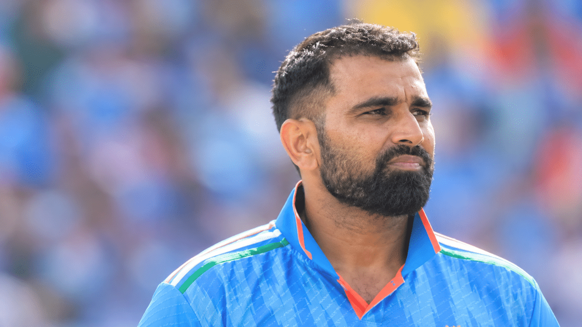 Mohammed Shami, Indian right-arm fast bowler, wearing a blue cricket jersey with orange collar accents and looking to the right against a blurred stadium background.